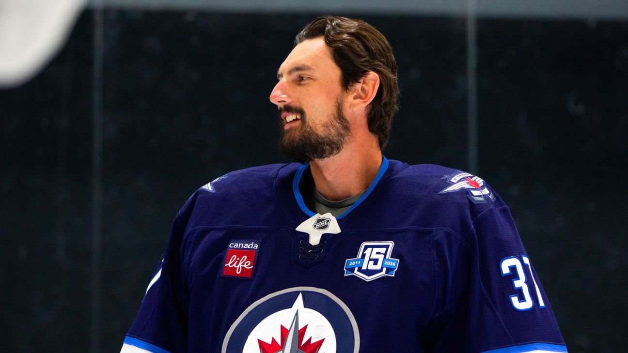 Connor Hellebuyck smiles while wearing a Winnipeg Jets sweater
