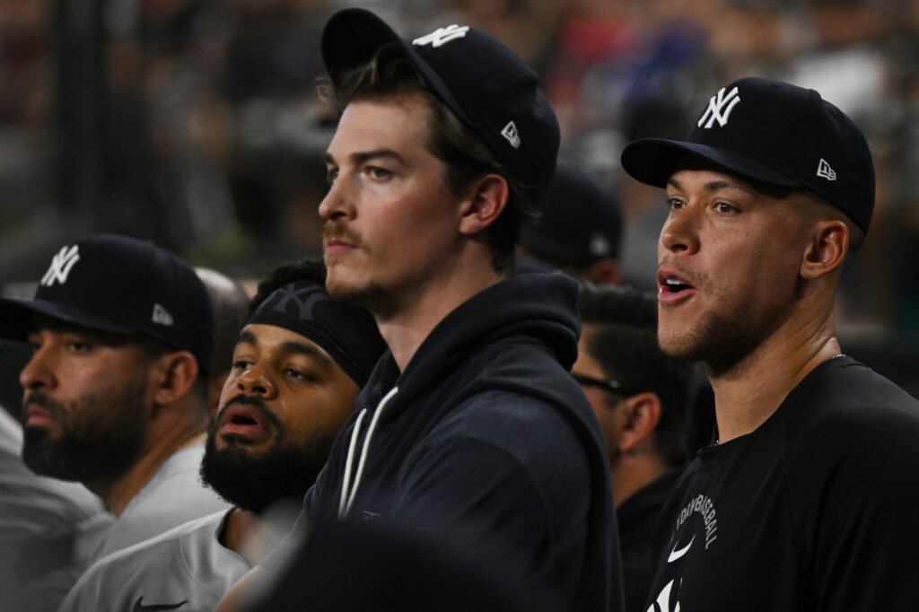 Aaron Judge stands at the right of a group of Yankees players watching from the dugout.