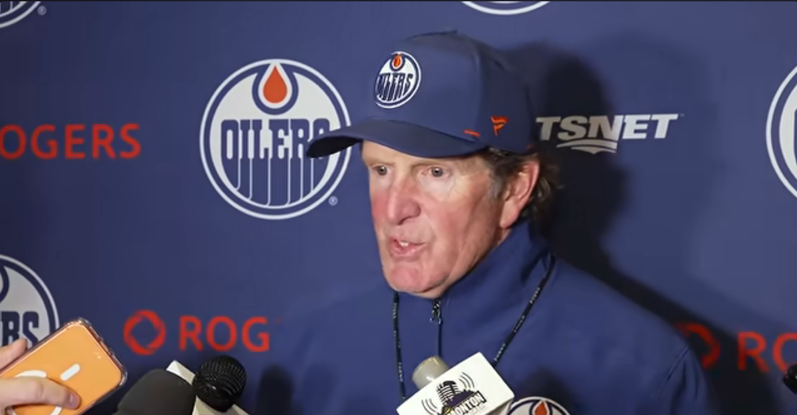 Mike Babcock speaks to reporters in front of an Edmonton Oilers backdrop.