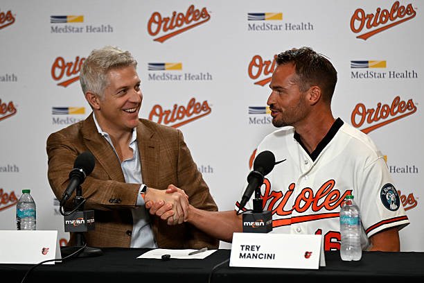 Trey Mancini shakes hands with Orioles executive Mike Elias after signing a one-day contract at Camden Yards.