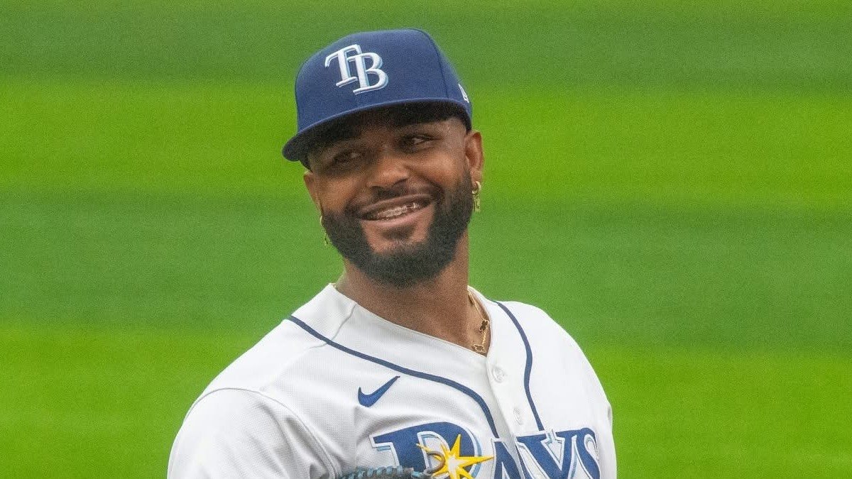 Junior Caminero smiling in a white Tampa Bay Rays uniform and navy cap.