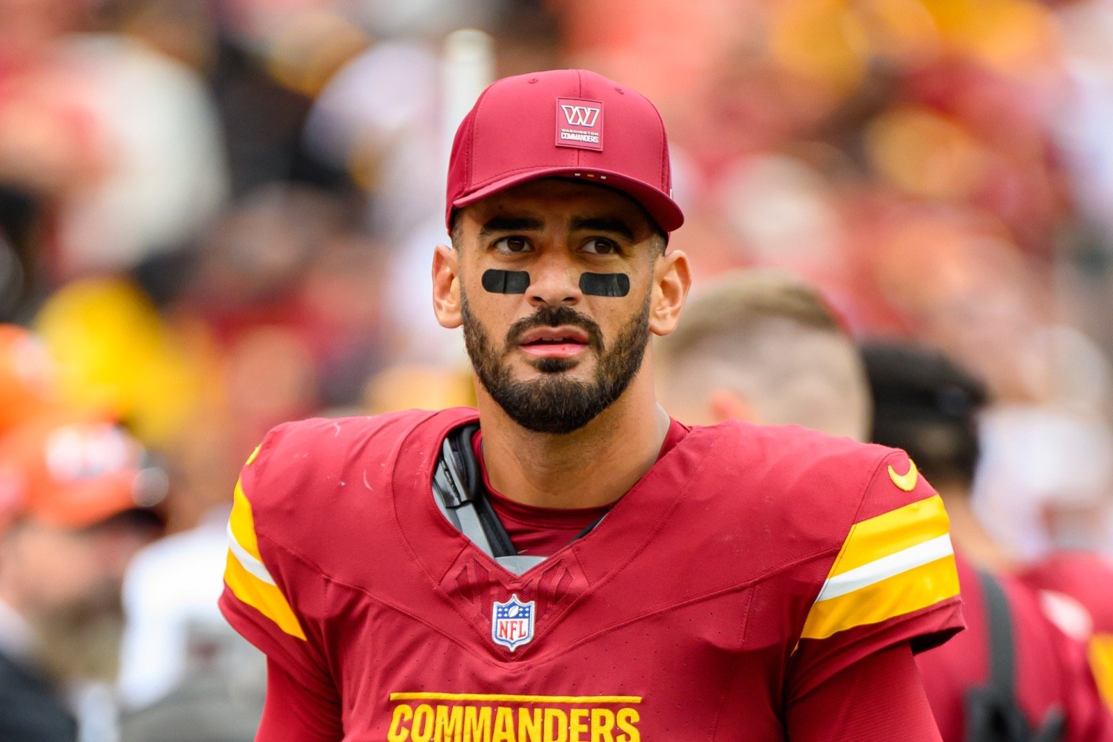 Marcus Mariota wearing a burgundy Washington Commanders jersey and cap on the sideline.
