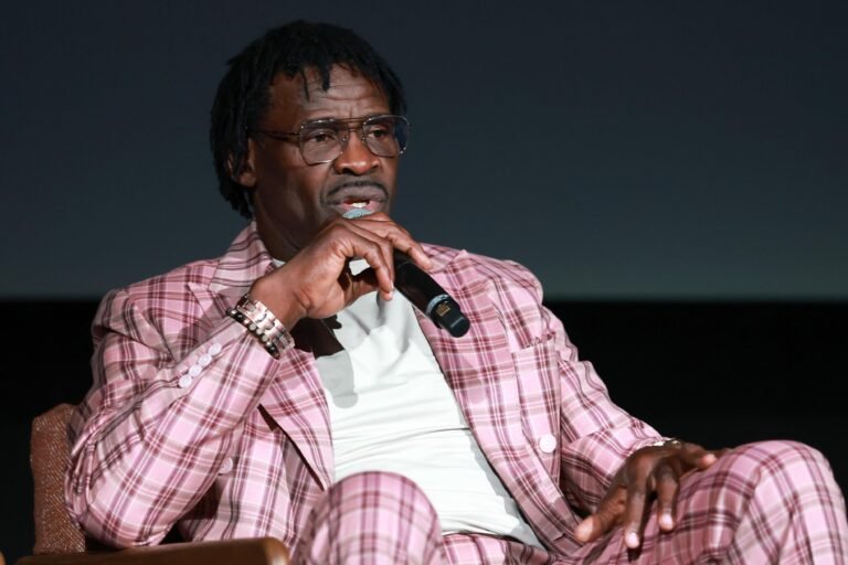 Michael Irvin holding a microphone while seated in a pink plaid suit.