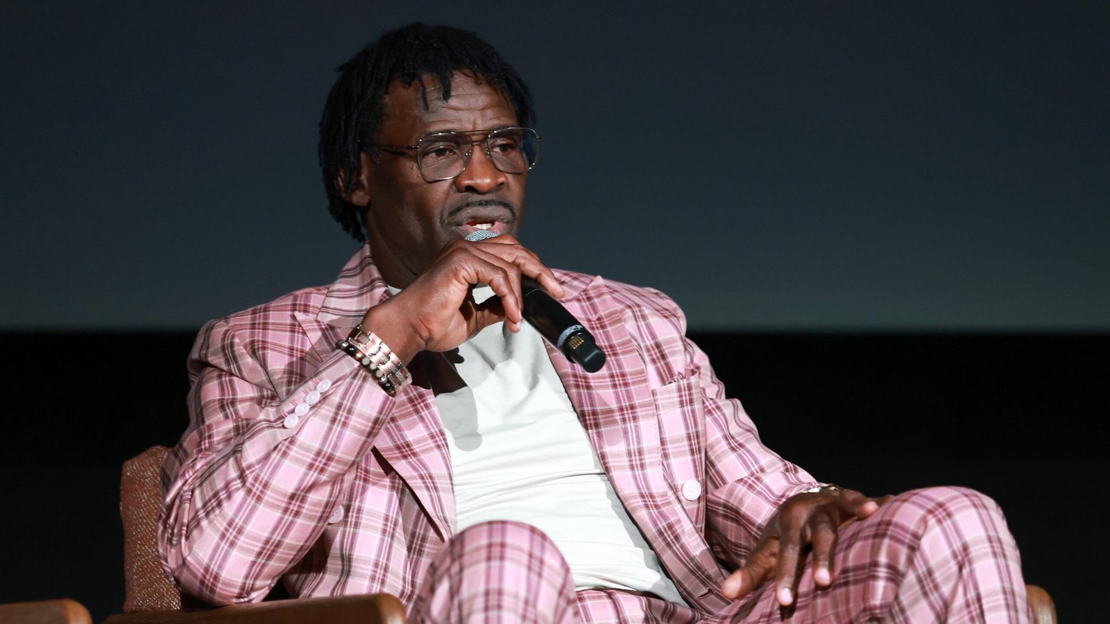 Michael Irvin holding a microphone while seated in a pink plaid suit.