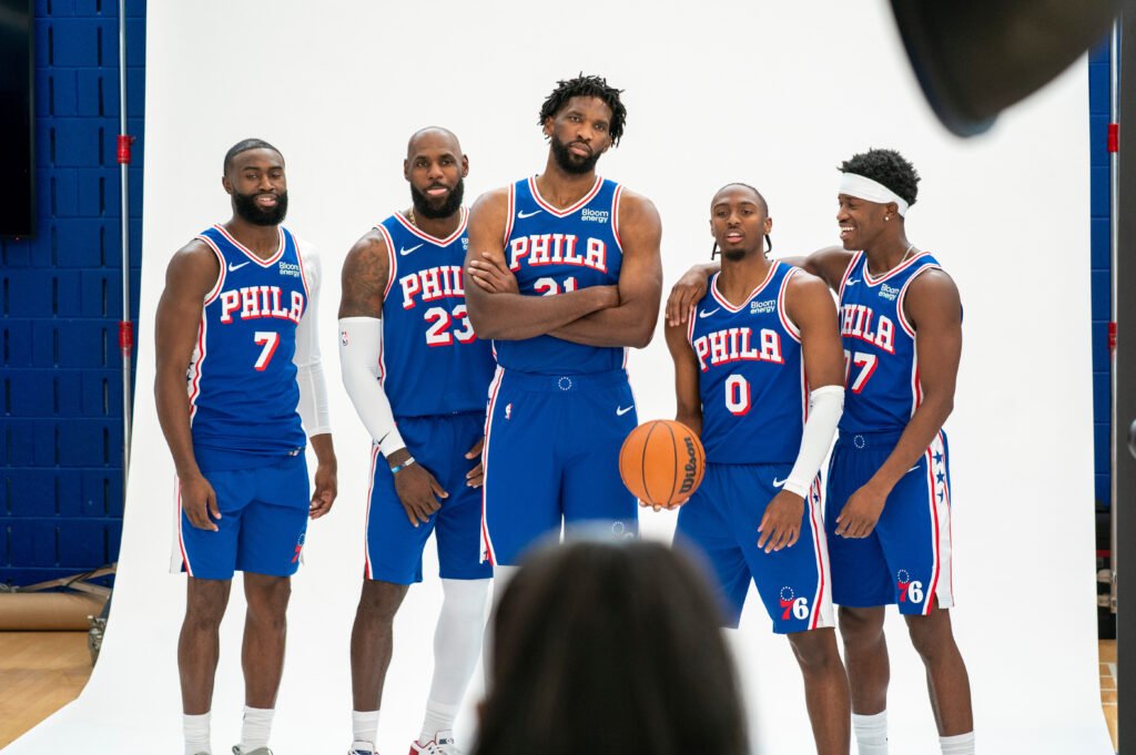 Jaylen Brown, LeBron James, Joel Embiid, Tyrese Maxey and VJ Edgecombe pose in blue Sixers uniforms at media day.