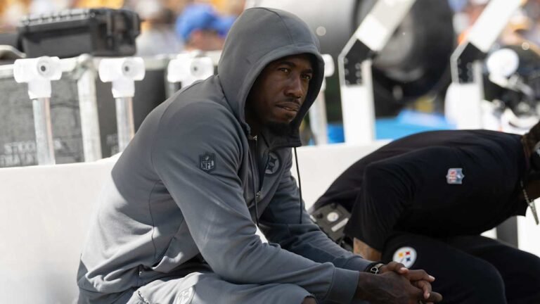 Joey Porter Jr. sits on the Steelers sideline wearing a gray hooded sweatshirt.