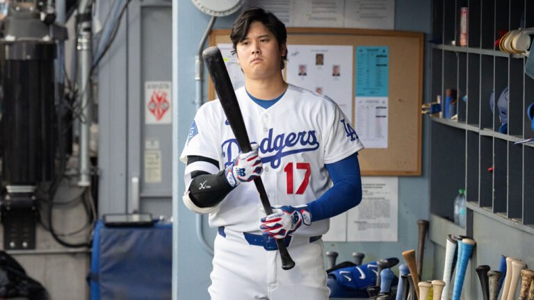 Shohei Ohtani holds a bat in the Dodgers dugout.