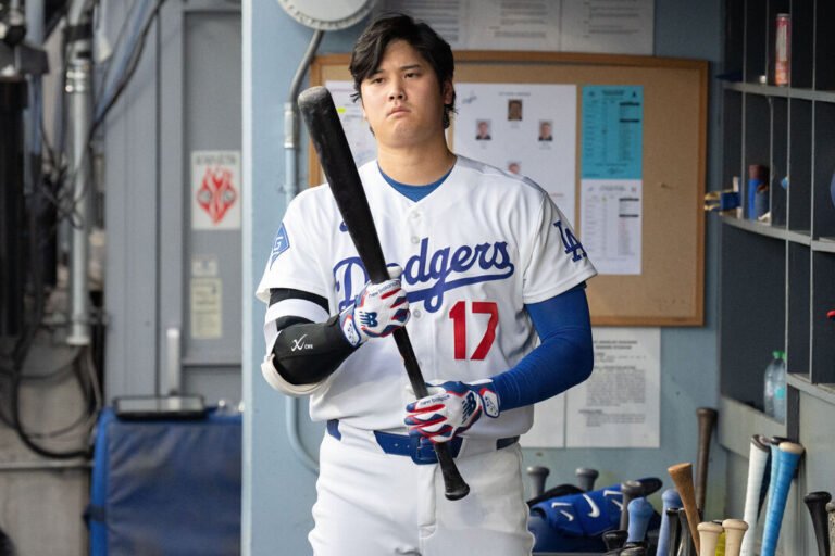 Shohei Ohtani holds a bat in the Dodgers dugout.