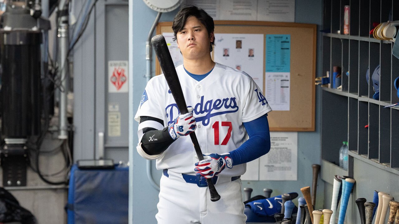 Shohei Ohtani holds a bat in the Dodgers dugout.