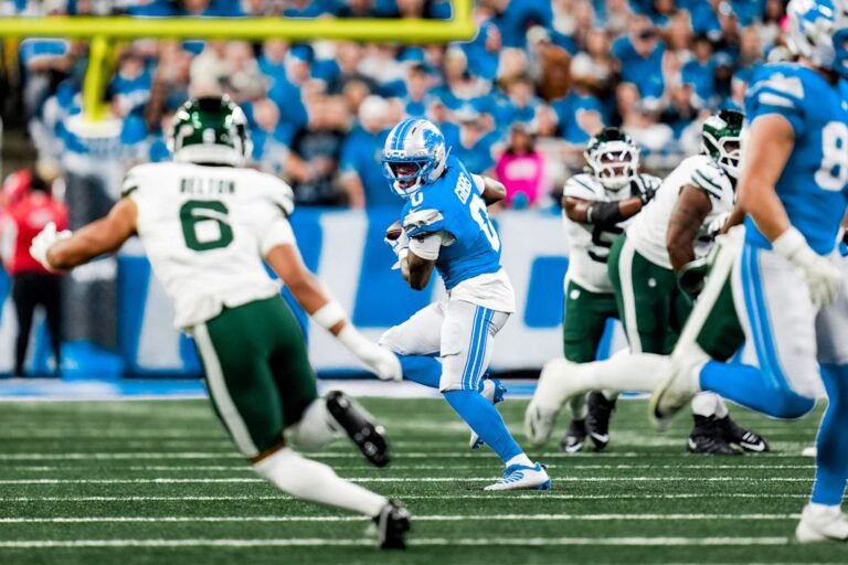 Jahmyr Gibbs runs with the ball as Jets defenders close in at Ford Field.
