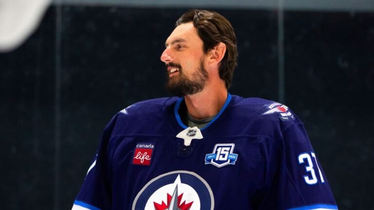 Connor Hellebuyck smiles while wearing a Winnipeg Jets sweater