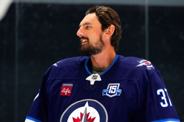 Connor Hellebuyck smiles while wearing a Winnipeg Jets sweater