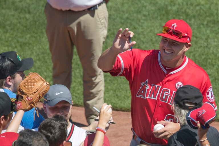 Mike Trout signs autographs for fans while wearing a red Angels uniform