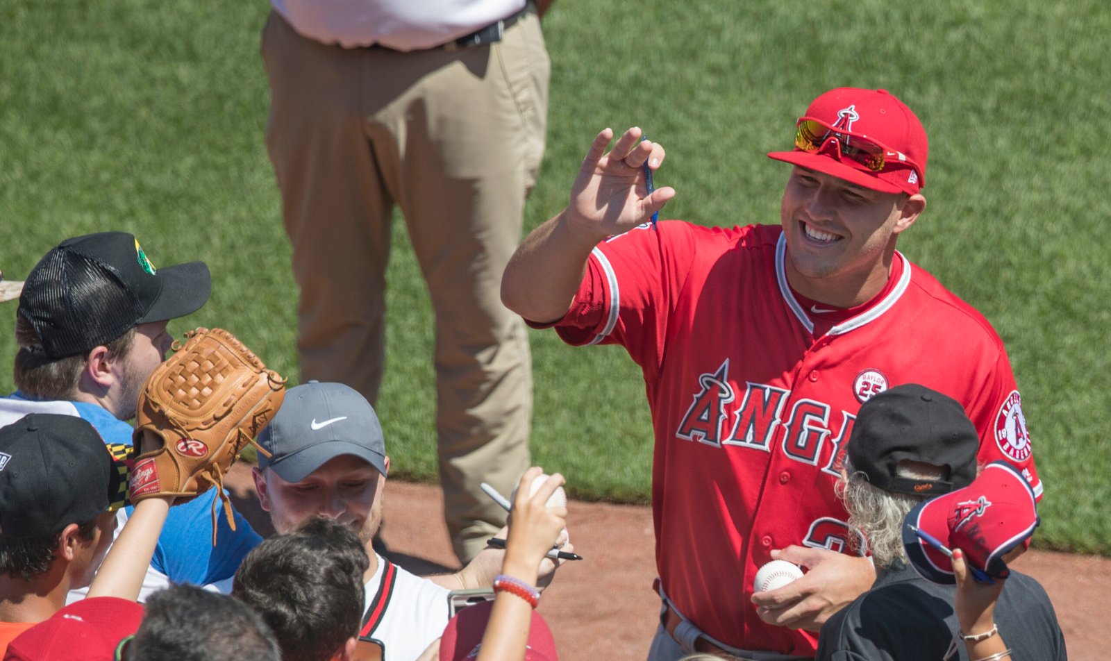 Mike Trout signs autographs for fans while wearing a red Angels uniform
