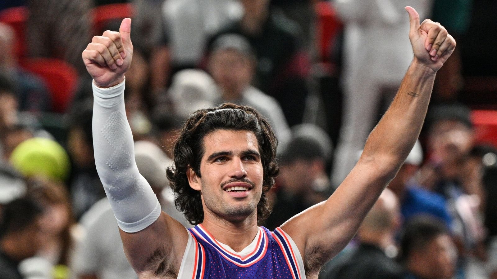 Carlos Alcaraz gives two thumbs up at a tennis tournament.