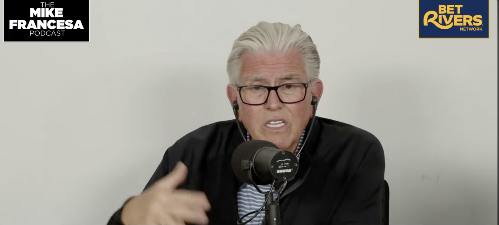 Mike Francesa, wearing glasses and earbuds, speaks into a microphone on his podcast.