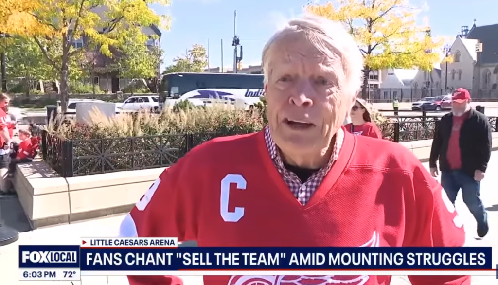 A Red Wings fan in a red captain’s jersey speaks outside Little Caesars Arena.