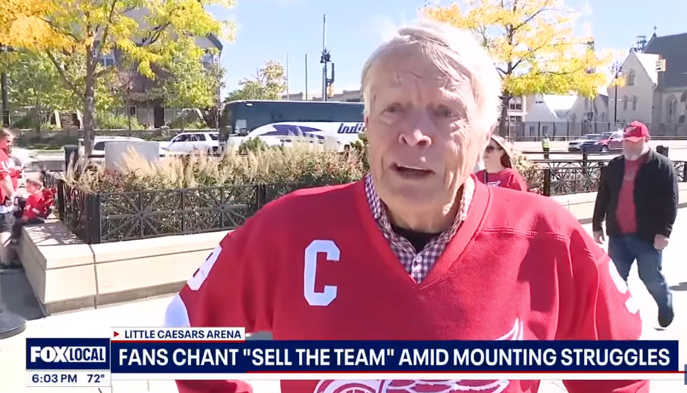 A Red Wings fan in a red captain’s jersey speaks outside Little Caesars Arena.