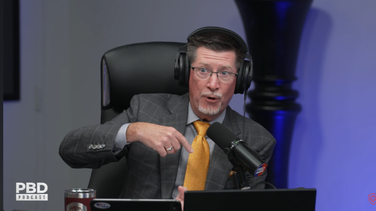 Tom Ellsworth in a gray suit and yellow tie speaking during the PBD Podcast discussion about Nike.