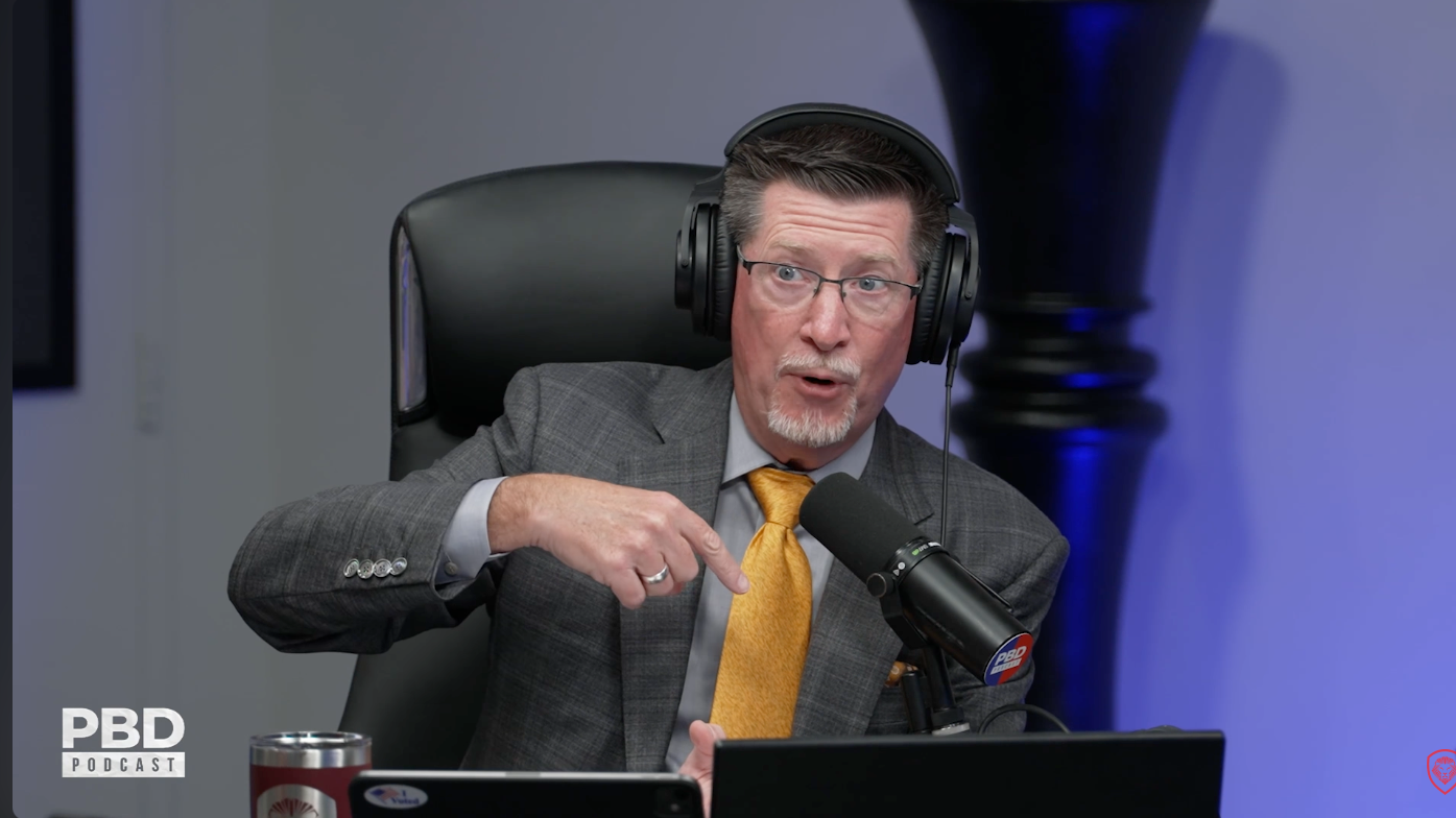 Tom Ellsworth in a gray suit and yellow tie speaking during the PBD Podcast discussion about Nike.