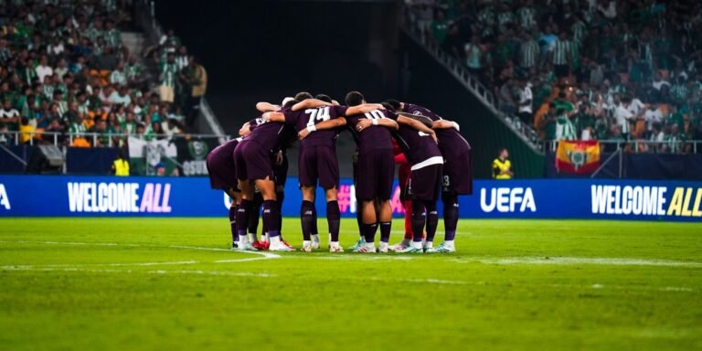 Porto players huddle in purple kits at La Cartuja, with Betis supporters behind them.