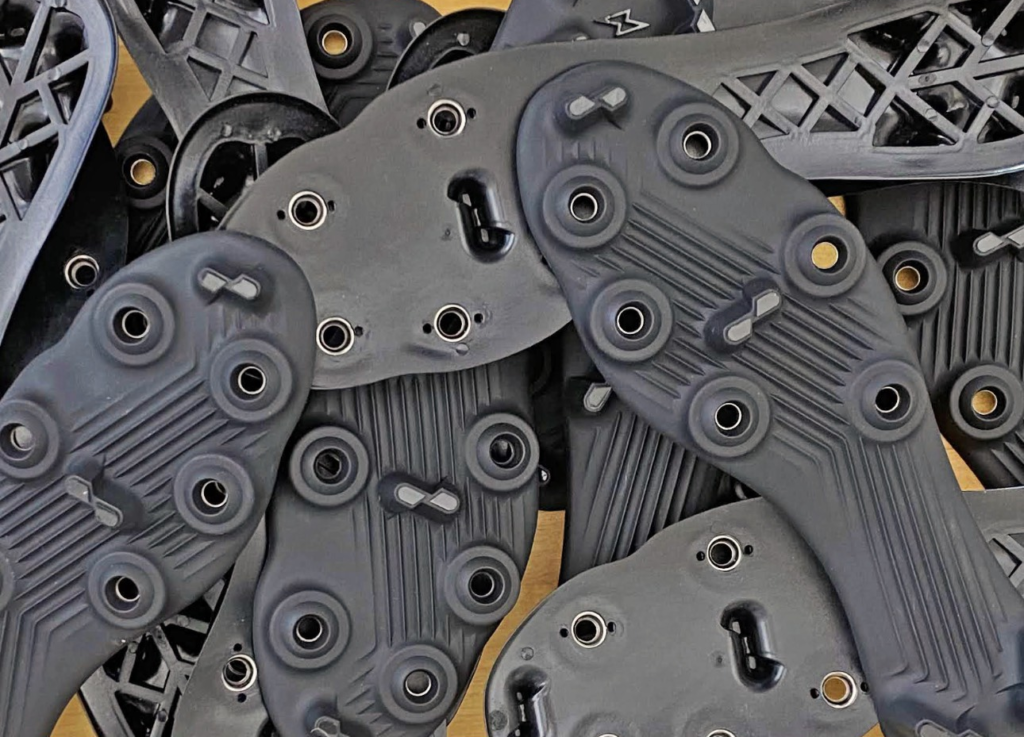 Several gray Caddix sole components with circular mounting points are stacked together on a work surface.