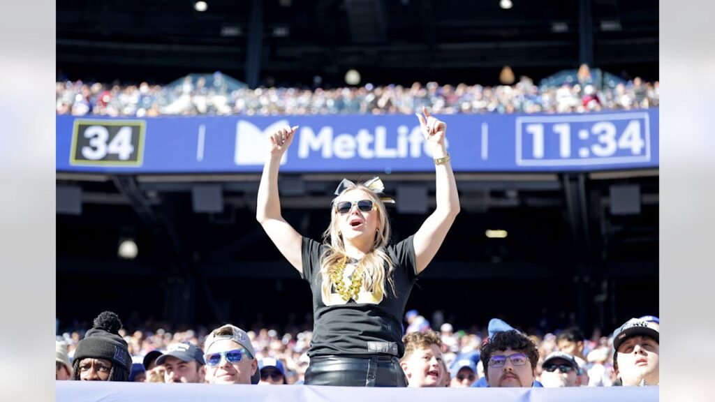 A Saints fan cheers in the MetLife Stadium stands, with stadium signage and other spectators behind her.