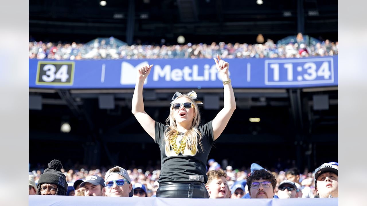 A Saints fan cheers in the MetLife Stadium stands, with stadium signage and other spectators behind her.