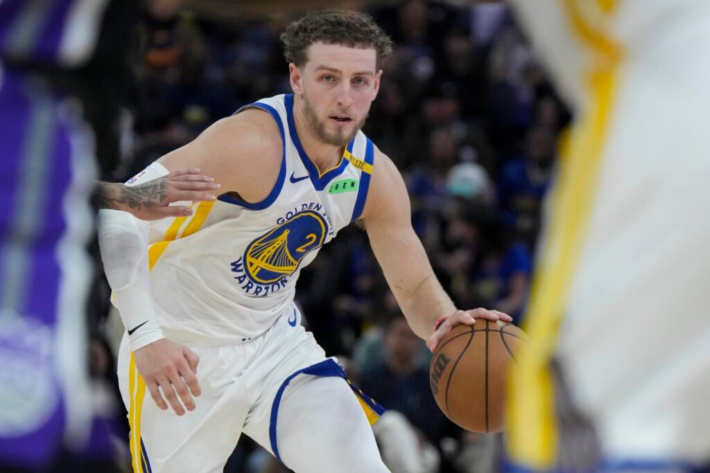 Brandin Podziemski dribbles in a white Golden State Warriors uniform during a preseason game against Sacramento.