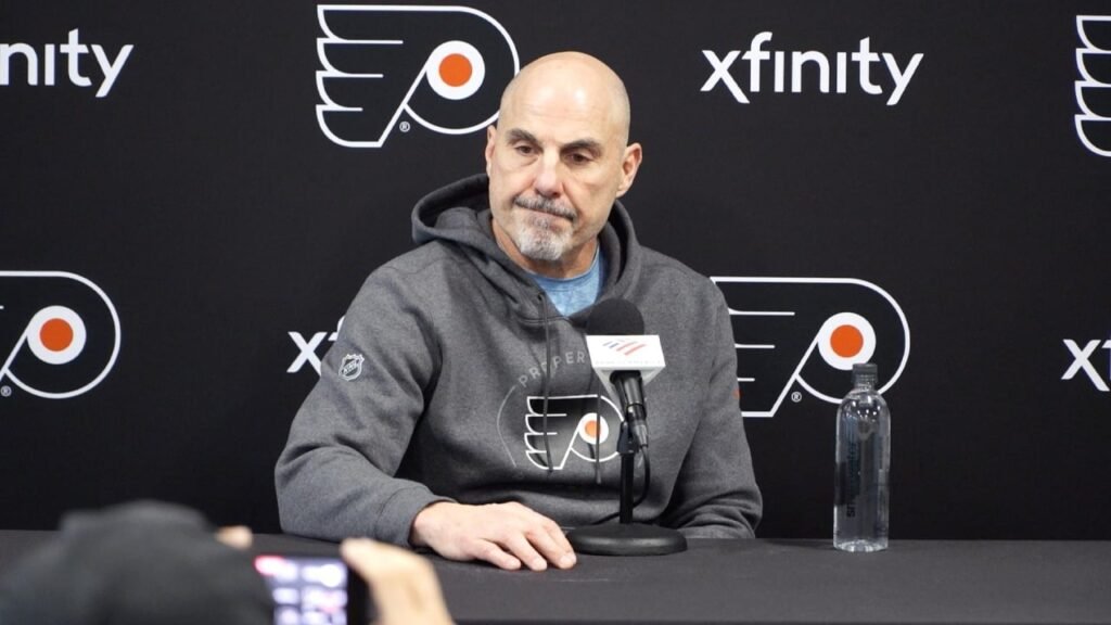 Rick Tocchet sits at a microphone in front of a Flyers backdrop after practice on October 18, 2026.