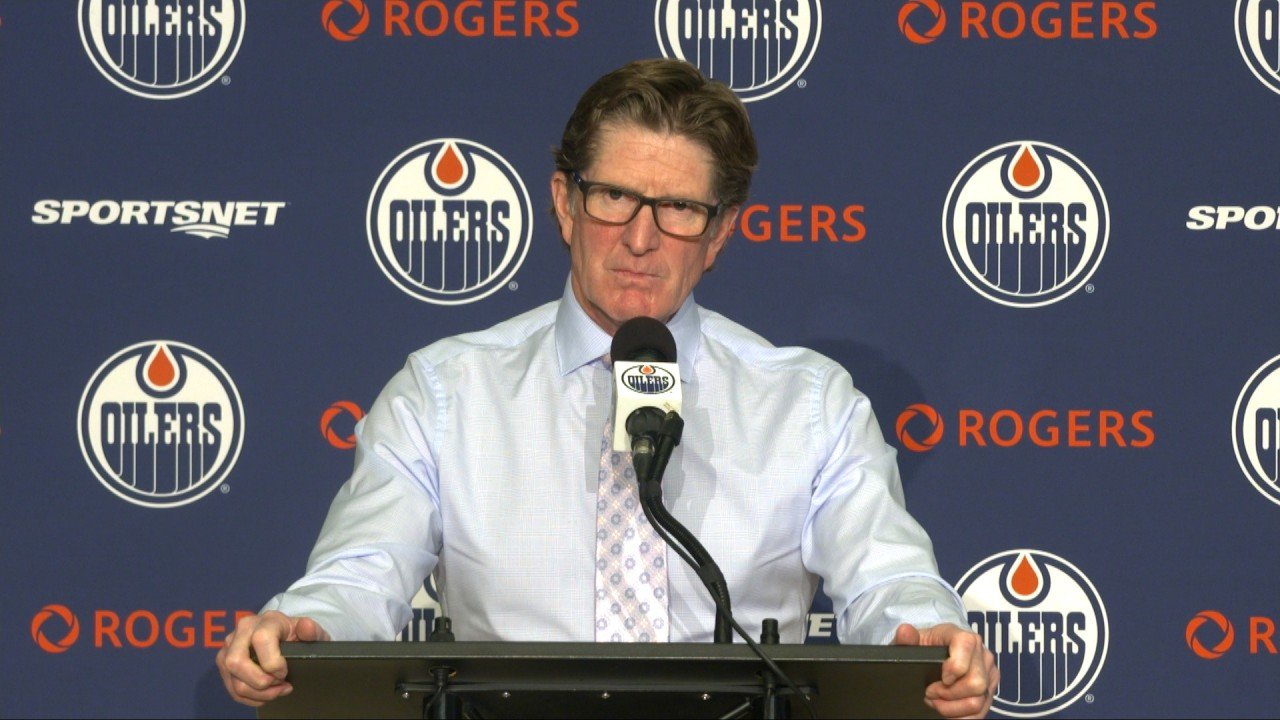 Mike Babcock speaks at a microphone in front of an Oilers backdrop.