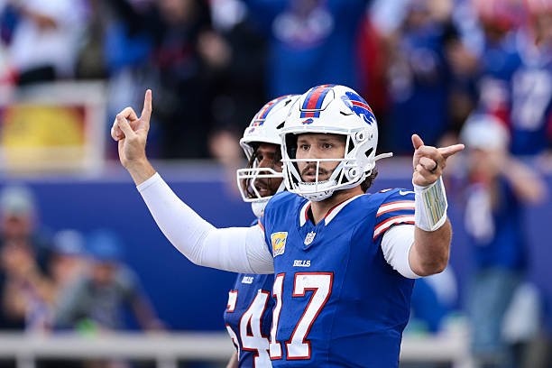 Josh Allen in a blue Bills uniform and helmet raises both hands against New England.
