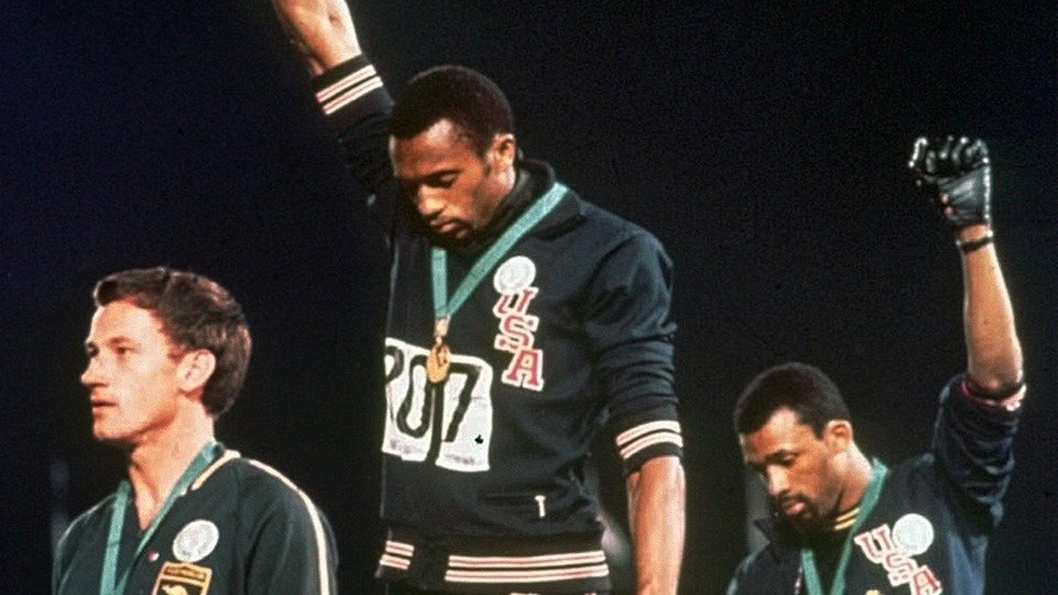 Tommie Smith and John Carlos raise gloved fists on the 1968 Olympic medal podium.