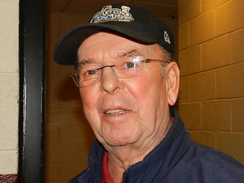 A portrait of Bob Cole wearing a Stanley Cup Playoffs cap.