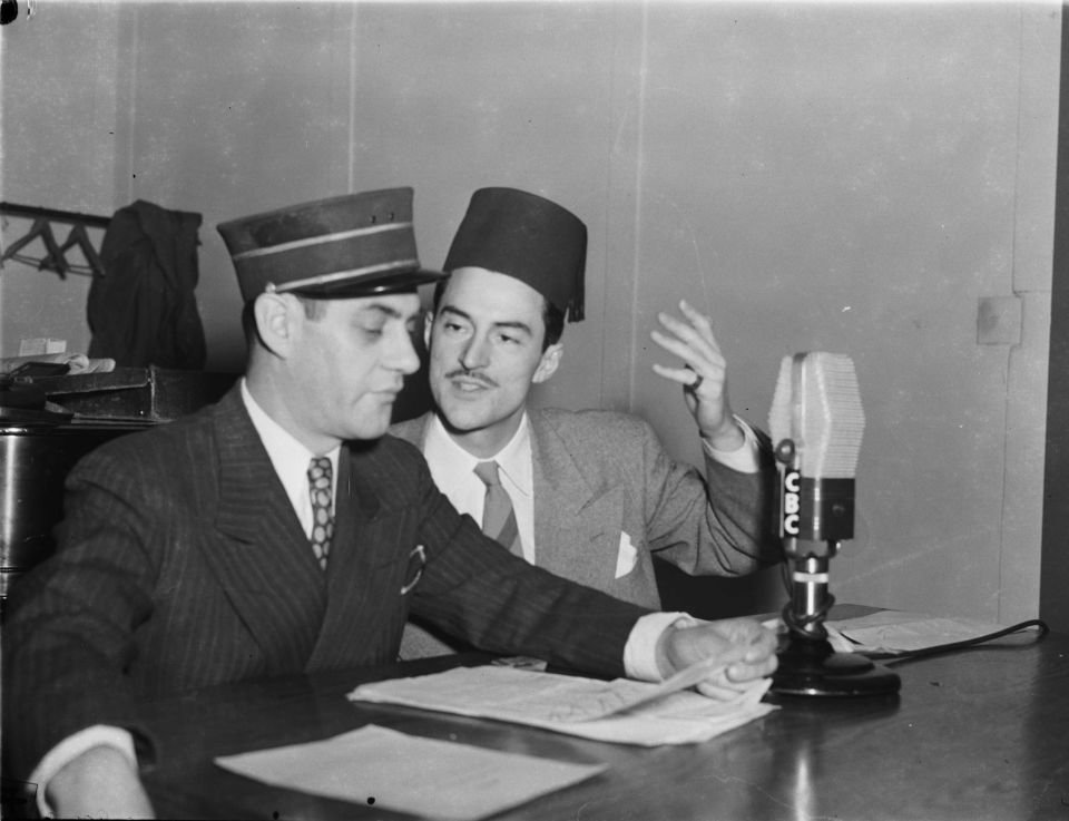 René Lecavalier and a colleague in costume speaking beside a CBC radio microphone.