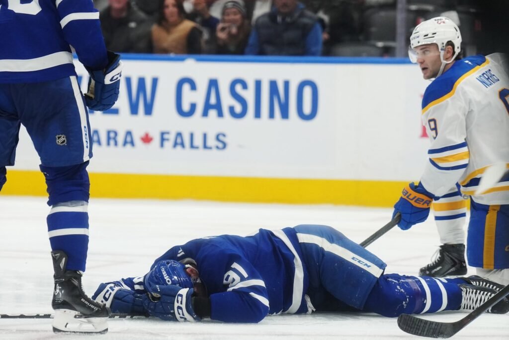 John Tavares in Toronto’s blue No. 91 jersey lies on the ice, with Buffalo’s Josh Norris beside him.