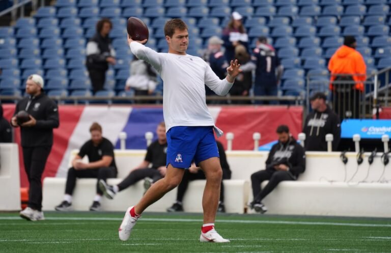 Drake Maye wearing a white warmup shirt and blue shorts while throwing before the October 11, 2026 game against Las Vegas at Gillette Stadium.