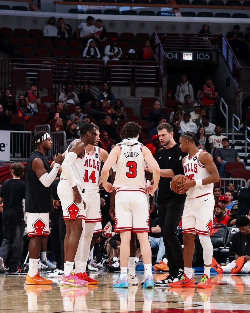 Chicago Bulls players gather around coach Tiago Splitter in a courtside huddle.