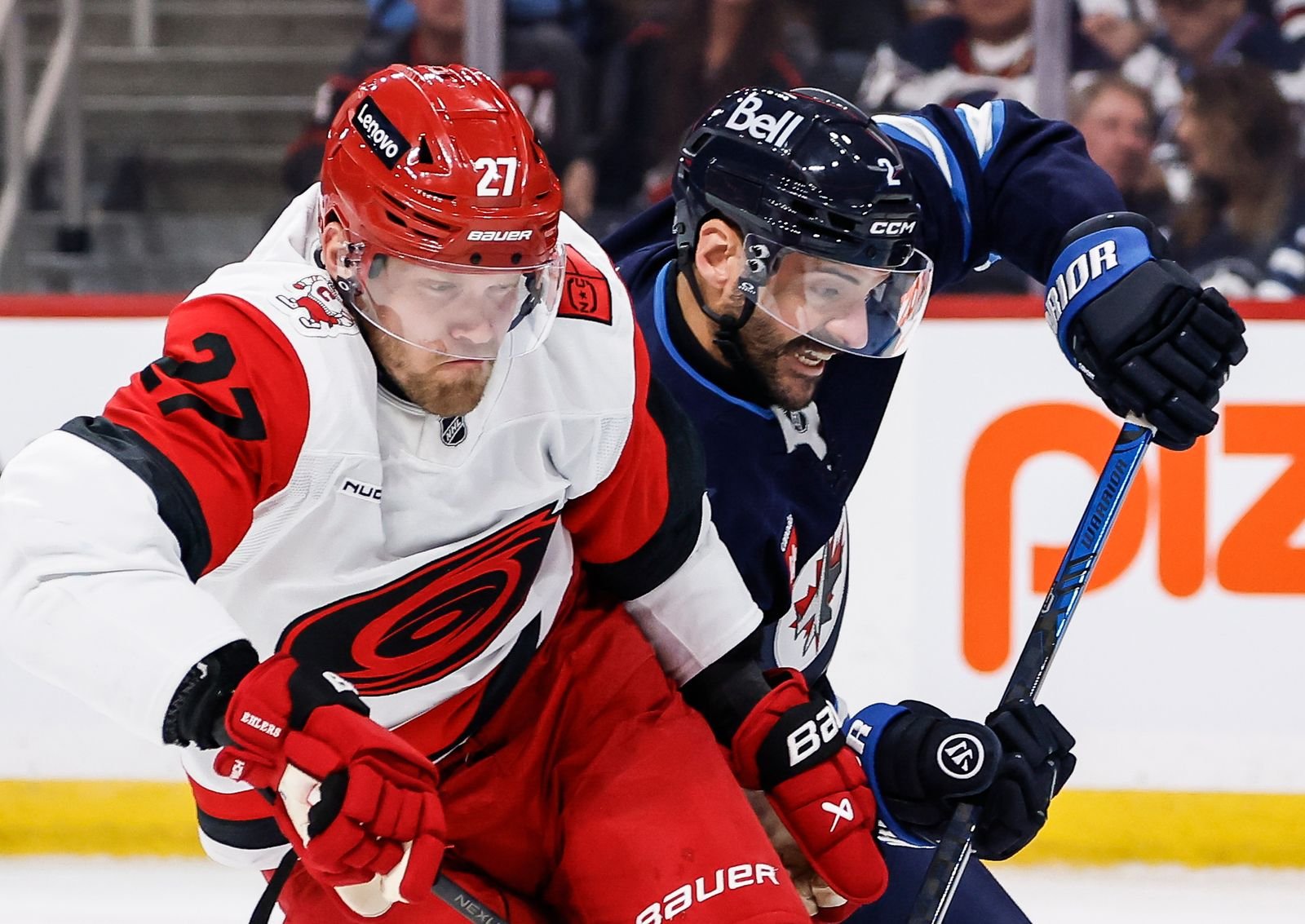 Nikolaj Ehlers, in a white Hurricanes jersey, battles Winnipeg defender Dylan DeMelo for the puck.