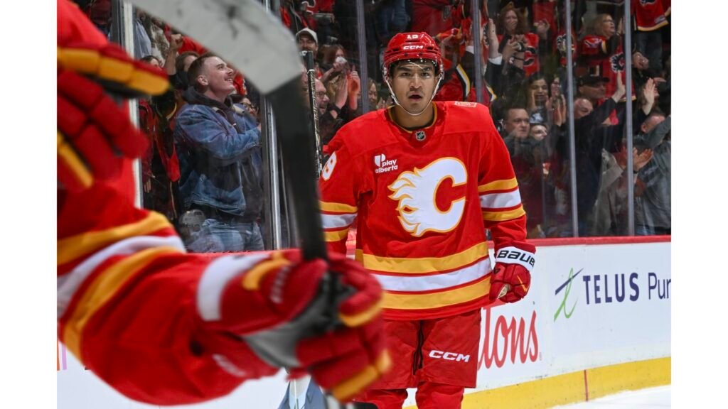 Zayne Parekh in a red Flames jersey beside the boards at Scotiabank Saddledome.
