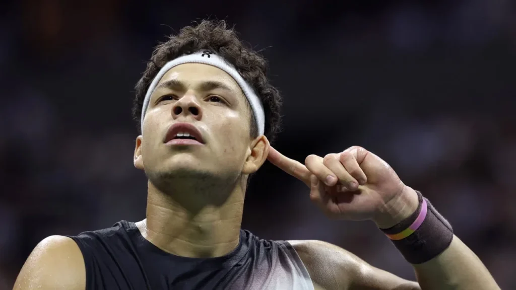 Ben Shelton gestures toward his ear while holding his racket.