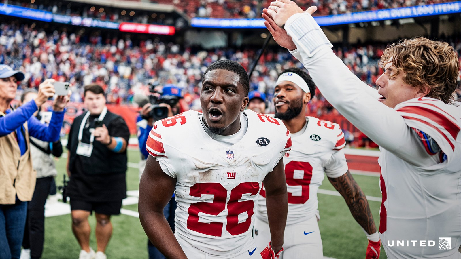 Devin Singletary, wearing the Giants’ white number 26 jersey, celebrates on the field with teammates in Houston.