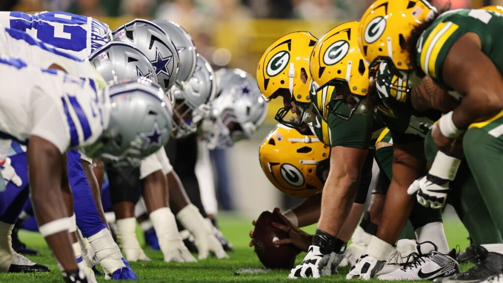 Cowboys and Packers helmets at the line of scrimmage at Lambeau Field.