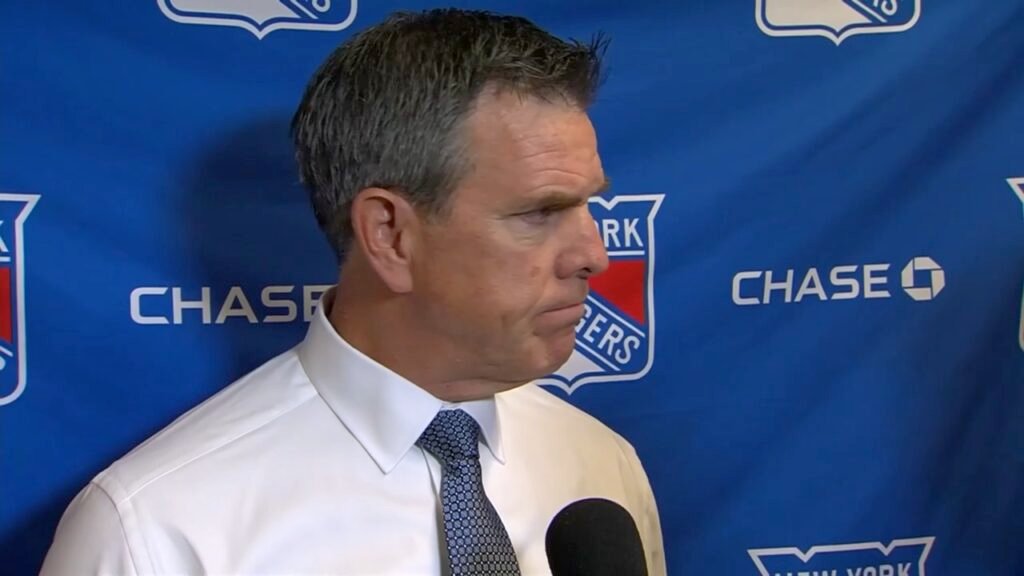 Mike Sullivan speaks at a microphone in a shirt and tie in front of a Rangers and Chase backdrop.
