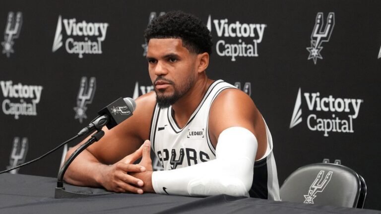 Tobias Harris answers questions at a microphone while wearing a Spurs jersey.