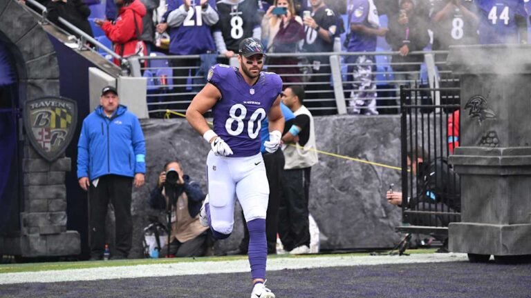 Durham Smythe wearing a purple Ravens No. 80 jersey as he runs onto the field.