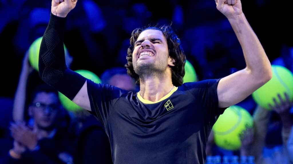 Carlos Alcaraz raises both fists while celebrating on an indoor tennis court.