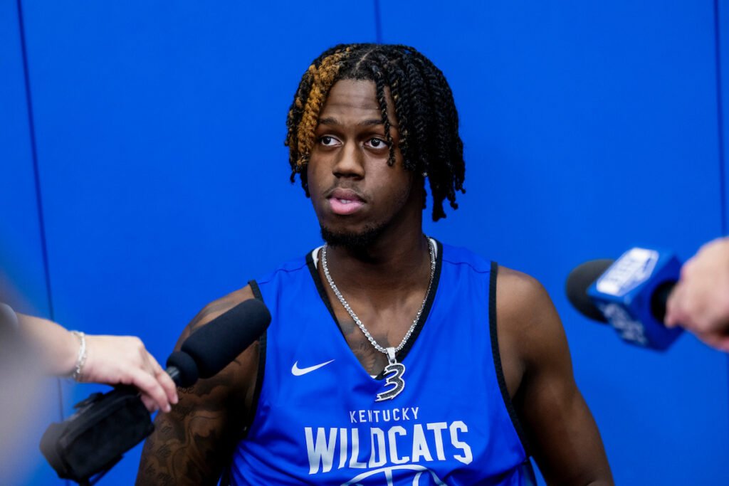Kam Williams sits before microphones in a blue Kentucky Wildcats practice jersey.