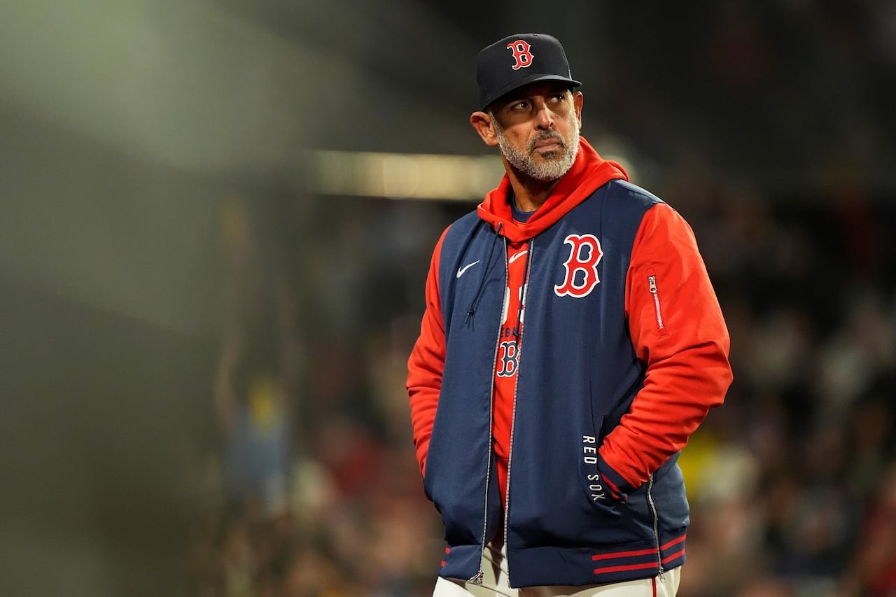 Alex Cora wears a Boston Red Sox cap and jacket on the field.