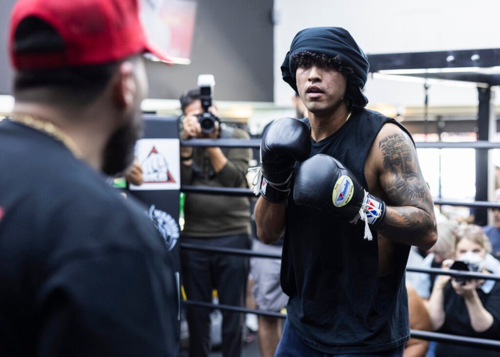 Anthony Vargas works out in boxing gloves with a trainer as photographers watch.
